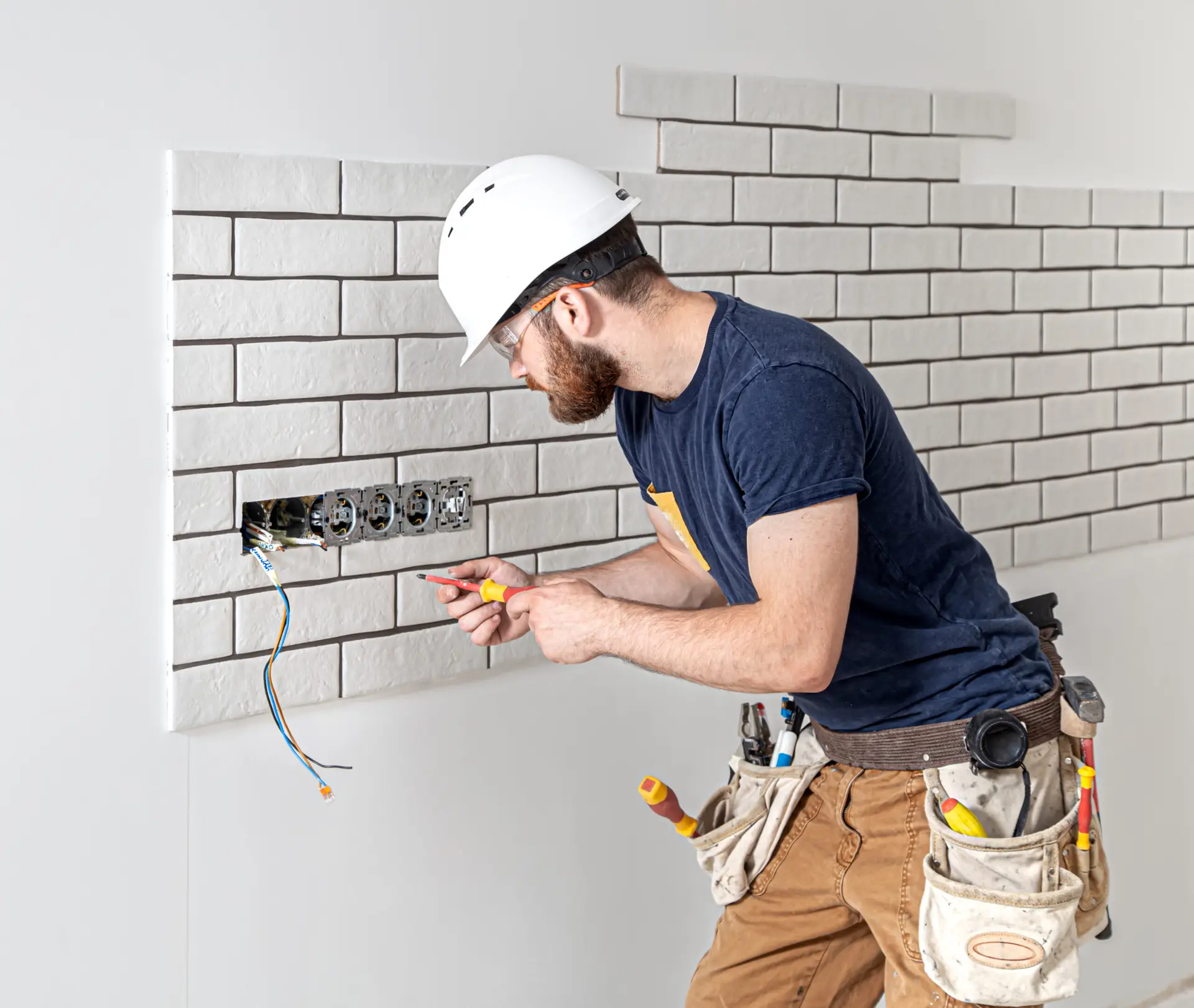 Electrician builder in a white helmet at work, installation of sockets, and switches.